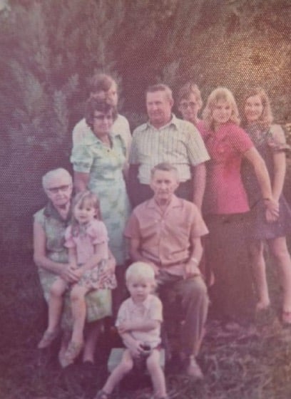 Foto familiar de los años 70: tres generaciones posan al aire libre; los mayores sentados, con dos niños pequeños adelante.