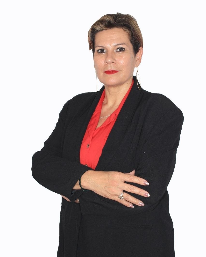 Retrato de Mariela Matthies, con saco negro y blusa roja, de brazos cruzados.
